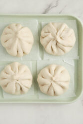 Four uncooked pork buns on parchment paper squares.