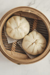 Two steamed pork buns in a bamboo steamer basket.