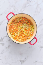 Sautéing vegetables for sausage and lentil soup in a red pot.