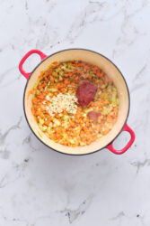 Stirring minced garlic and tomato paste into diced vegetables for sausage and lentil soup.