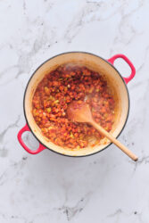 Sautéing vegetables in a red pot for sausage and lentil soup.