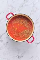 Combining broth, tomatoes, lentils, and seasonings for sausage and lentil soup in a pot.
