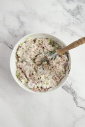 Seasoning the tuna melt mixture with salt and pepper in a white bowl.
