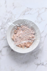Deviled ham in a bowl, covered with plastic wrap, on a marble counter.