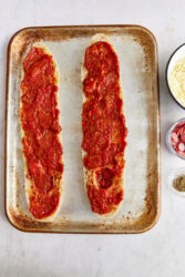 Spreading pizza sauce on baguette halves for pizza bread.